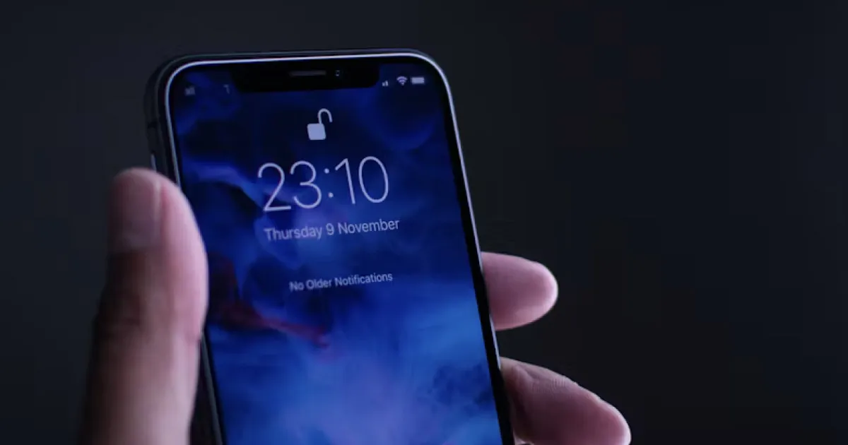 A hand holds an iPhone showing a blue lock screen with the time 23:10.