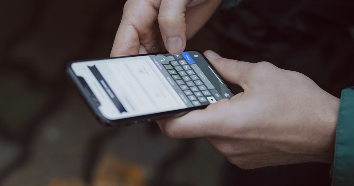 Two hands typing on the keyboard of an iPhone held sideways.