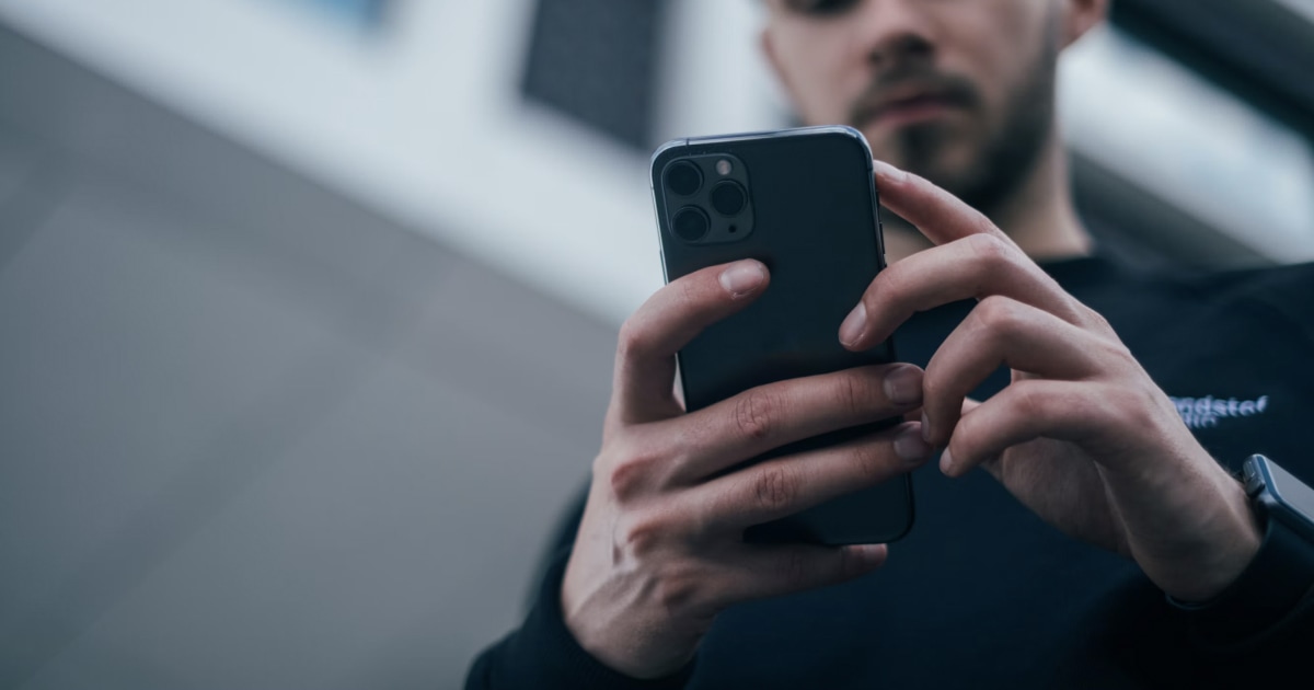 A man looks at an iPhone held in both hands, seen from a low angle.